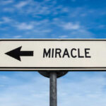 Road sign pointing left saying miracle
