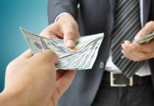 A person handing over a stack of cash to another individual in a suit