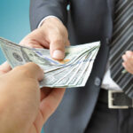 A person handing over a stack of cash to another individual in a suit
