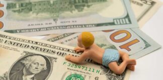 A baby figurine crawling on top of various dollar bills