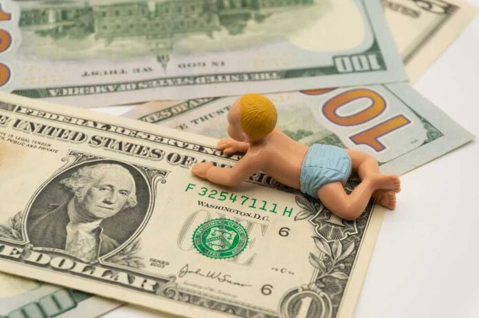 shutterstock_2143509017.jpg A baby figurine crawling on top of various dollar bills