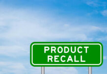 Green sign with product recall text and sky background