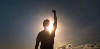 Silhouette of person with raised fist against sunset.