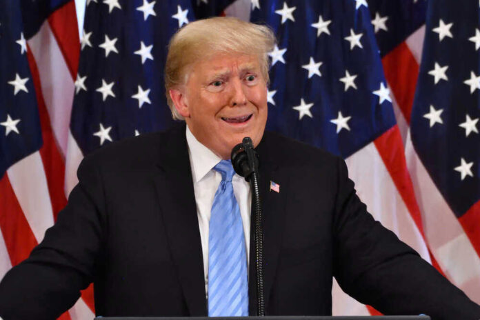 Man speaking at podium with American flags background.