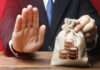 Businessman holding a money bag with a raised hand signaling refusal