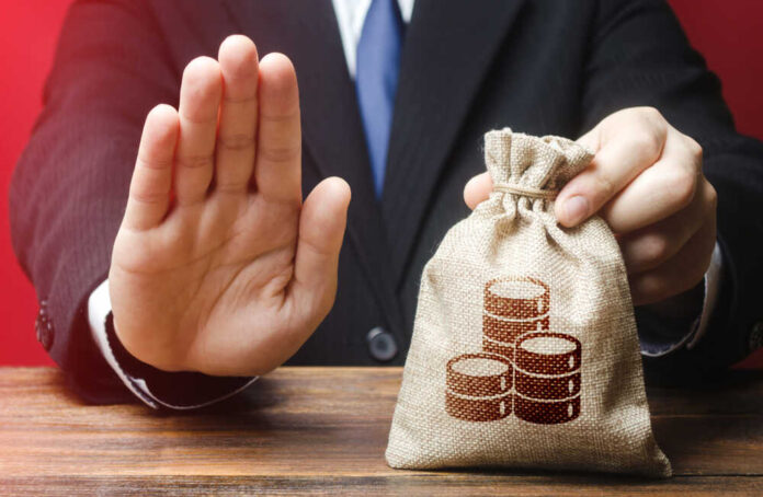 Businessman holding a money bag with a raised hand signaling refusal
