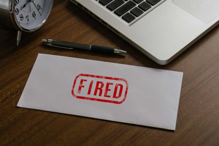 shutterstock_2188066111.jpg An envelope marked 'FIRED' on a wooden desk next to a clock and a laptop