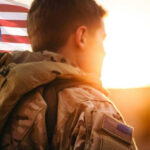 1,500 Troops READY — Tension Soars Soldier in uniform with American flag at sunset.