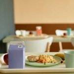 A tray with a healthy school lunch including a meat patty, rice, an apple, a banana, and a drink