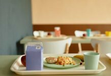 A tray with a healthy school lunch including a meat patty, rice, an apple, a banana, and a drink