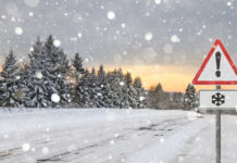 Snow-covered road with a warning sign and pine trees in the background