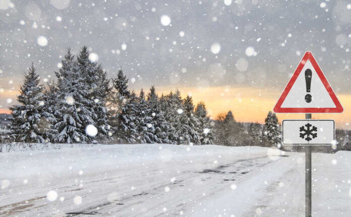 Snow-covered road with a warning sign and pine trees in the background