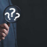 Hand holding magnifying glass with question marks inside.