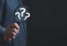 Hand holding magnifying glass with question marks inside.