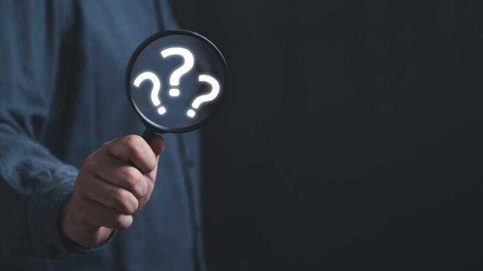 shutterstock_22781366671.jpg Hand holding magnifying glass with question marks inside.