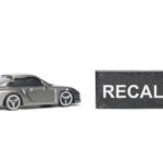A miniature gray sports car next to a black sign that reads 'RECALL'