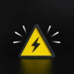 A yellow triangular warning sign with a lightning bolt on a black background