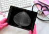 A person in pink gloves holding a tablet displaying a mammogram image