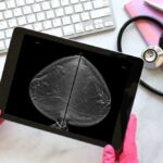 Breast Cancer Deaths PLUMMET — America’s Big Win A person in pink gloves holding a tablet displaying a mammogram image