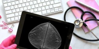 A person in pink gloves holding a tablet displaying a mammogram image