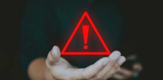A hand holding a red warning triangle with an exclamation mark