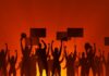 Silhouetted crowd of protesters holding signs against a fiery background
