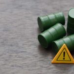 Four green barrels and a warning sign on a wooden surface