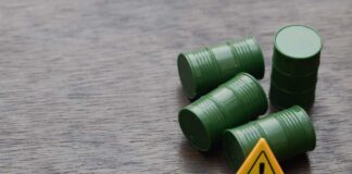 Four green barrels and a warning sign on a wooden surface