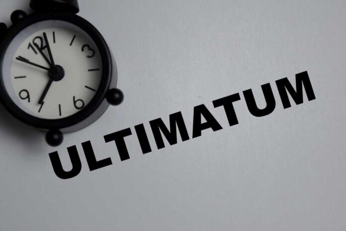 shutterstock_2703698743.jpg A black alarm clock next to the word 'ULTIMATUM' on a gray background