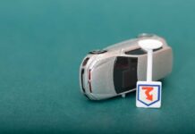 A silver toy car next to a small road sign