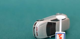 A silver toy car next to a small road sign