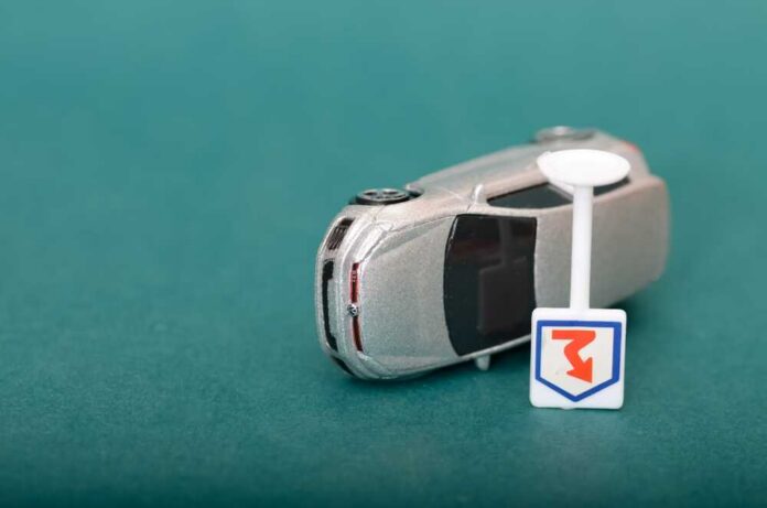 A silver toy car next to a small road sign