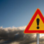 Massive Crackdown: 200,000 Truck Drivers at Risk A triangular warning sign with an exclamation mark against a cloudy sky