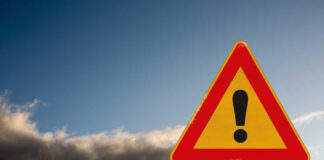 A triangular warning sign with an exclamation mark against a cloudy sky