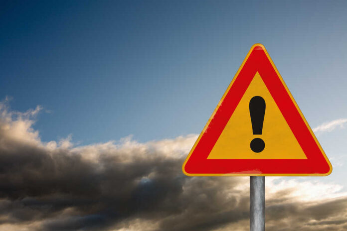 A triangular warning sign with an exclamation mark against a cloudy sky