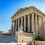 Supreme Court Bombshell: Bannon Conviction Erased? Stone building with columns and statues, clear blue sky.