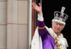 Man in royal attire and crown waving, stone background.