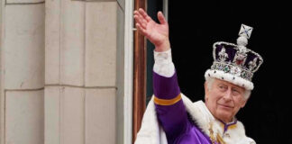 Man in royal attire and crown waving, stone background.
