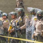 Line of police officers in riot gear standing behind shields