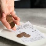 DELIVERY FEE Message Sparks Tipping Revolt Hand holding coins above a receipt on a plate