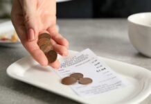 Hand holding coins above a receipt on a plate