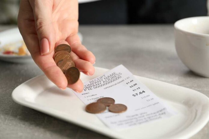 Hand holding coins above a receipt on a plate
