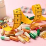 Assorted pills and a measuring tape on a pink background