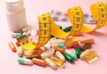 Assorted pills and a measuring tape on a pink background