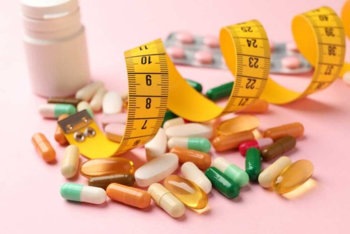 Assorted pills and a measuring tape on a pink background