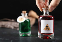 A hand holding a glass bottle labeled with a poison symbol, next to another bottle