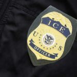 ICE Agent Charged In Bombshell Indictment Close-up of an ICE officer badge on a black jacket