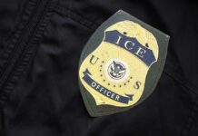 ICE Agent Charged In Bombshell Indictment Close-up of an ICE officer badge on a black jacket