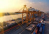Shipping containers and cranes at a port during sunset.