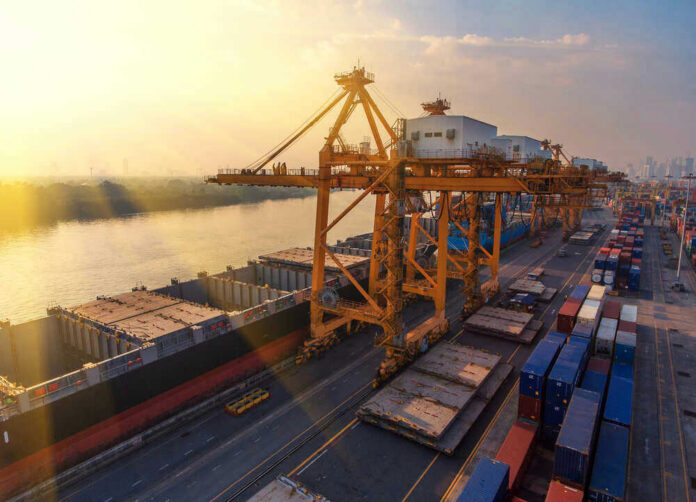 Shipping containers and cranes at a port during sunset.